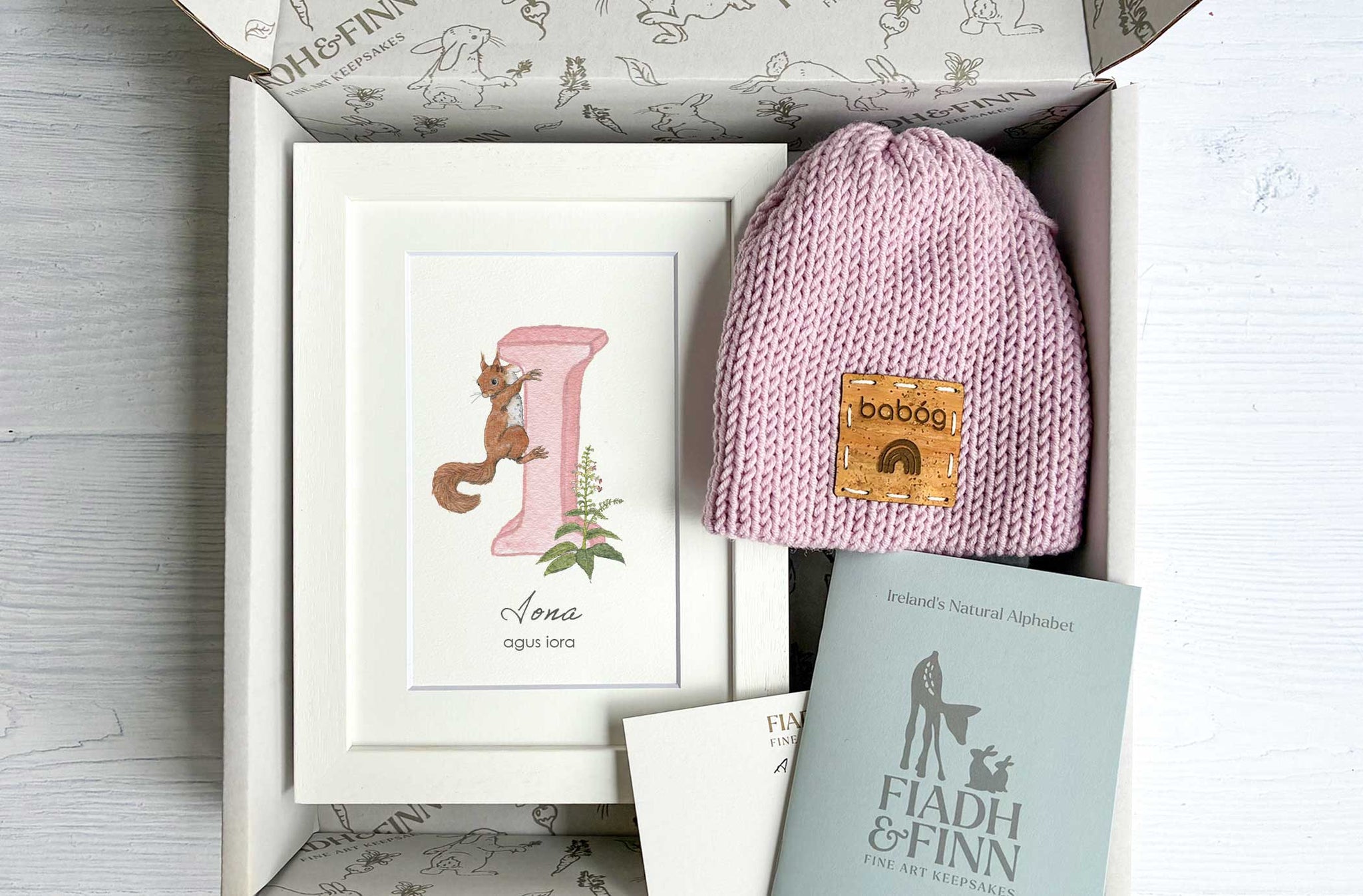 Baby gift set with pink beanie, framed artwork, and book in a box
