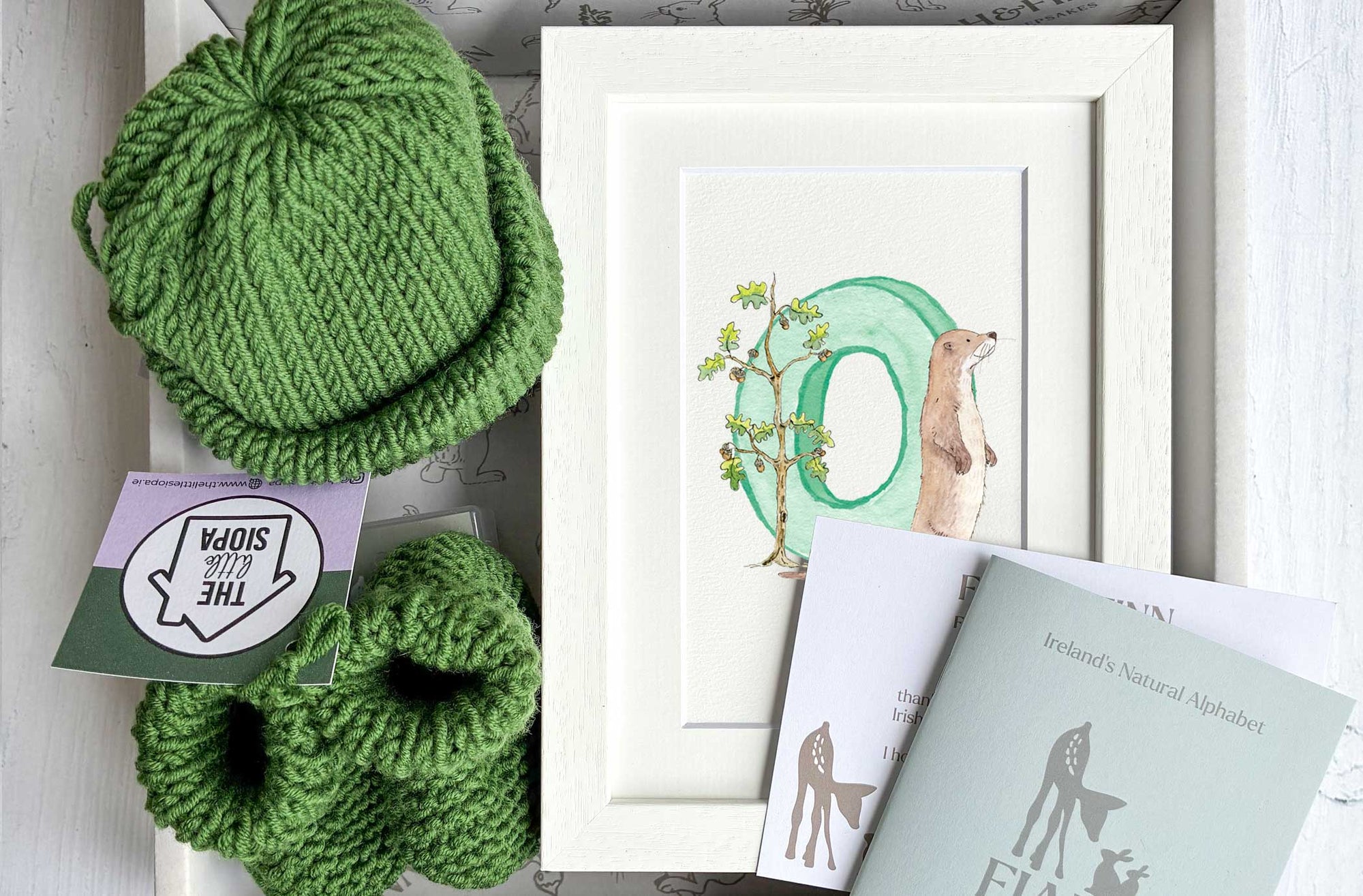 Green knitted baby hat and baby booties with white frames initial letter. Baby gift box set.