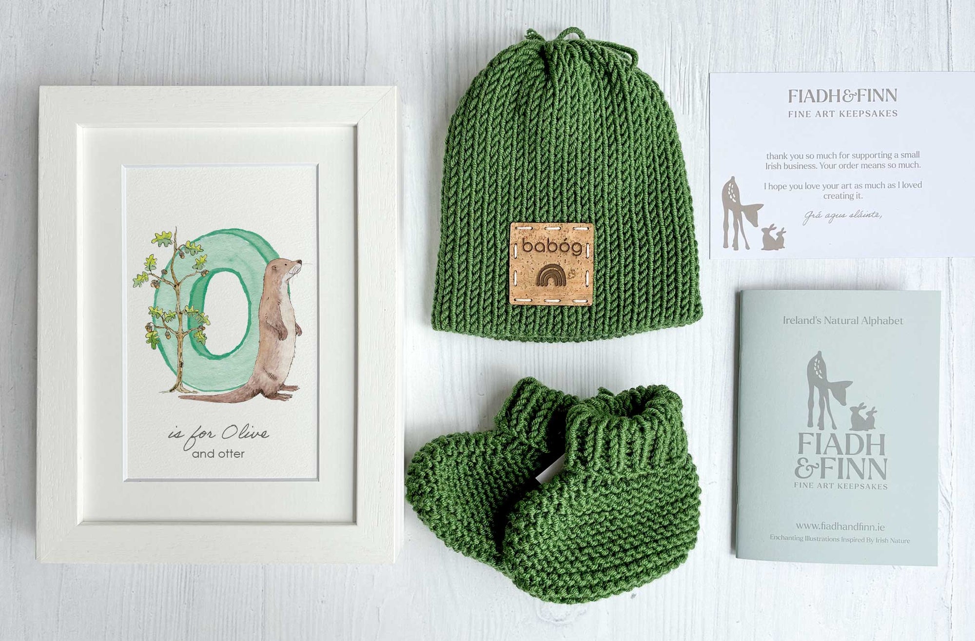 Green knitted baby hat and baby booties with white frames initial letter. Baby gift box set.