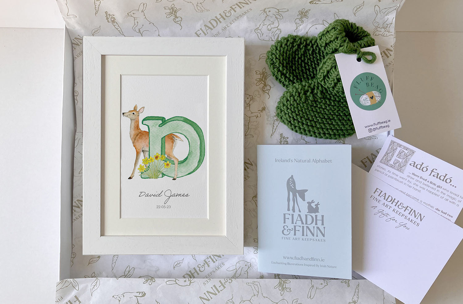Green knitted baby booties with white frames initial letter. Baby gift box set.